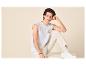 Jonge man in een wit mouwloos T-shirt met palmboomprint en beige broek.