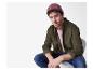 Homme en bonnet rose, chemise verte et jean assis sur une chaise.