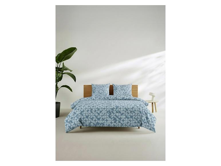 Parure de lit à motif géométrique sur un lit avec tête de lit en bois, à côté d'une plante et d'une table de chevet.