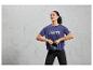 Une femme portant un t-shirt de sport bleu avec l'inscription 'Break the Limits' tient un kettlebell noir.