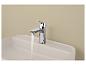 Robinet chromé avec de l'eau qui coule sur un lavabo rectangulaire blanc contre un mur beige.