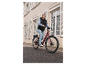 Vrouw lacht terwijl ze op een bordeauxrode elektrische fiets fietst.