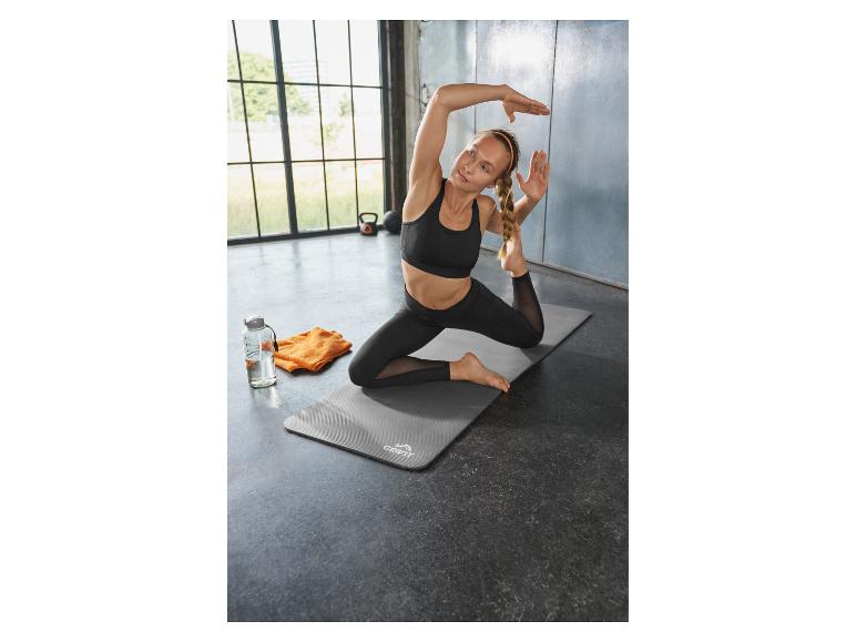 Vrouw doet yoga op een mat, met een waterfles en handdoek ernaast.