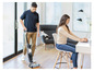 Un homme aspire avec un aspirateur Dyson sans fil tandis qu'une femme travaille sur un ordinateur portable.