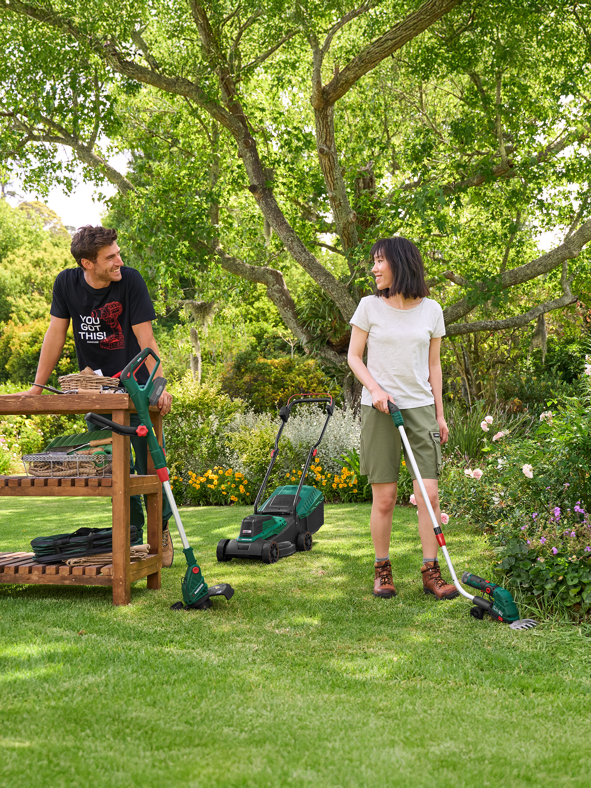 Homme et femme dans un jardin avec une tondeuse, un coupe-bordure et des cisailles à gazon.