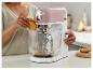 Une femme met des biscuits dans un robot pâtissier rose et blanc sur un comptoir de cuisine.