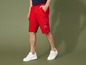 Man draagt rode cargo shorts met 'Miss Nature Company' logo en witte sneakers.