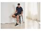 Homme en tenue de sport assis sur un tabouret utilisant un pistolet de massage sur sa cuisse.