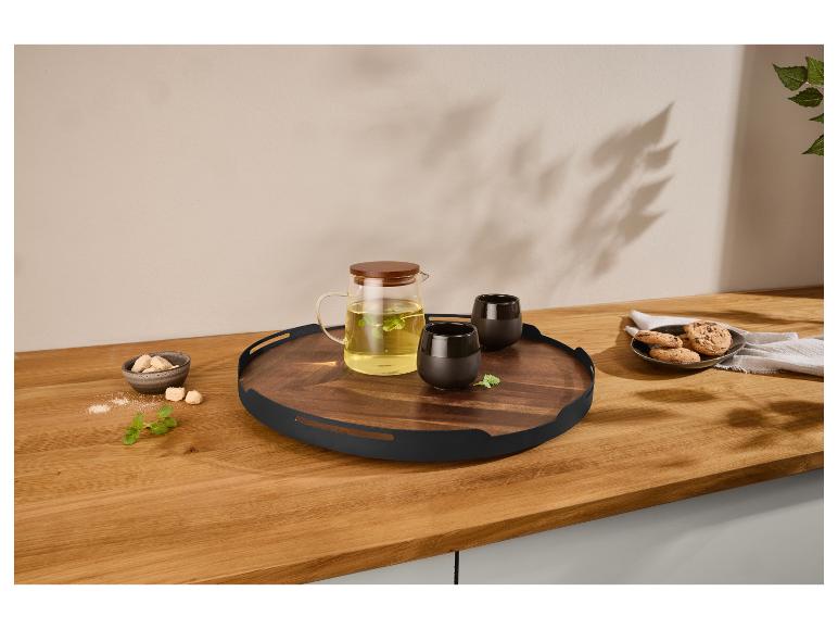 Plateau en bois avec théière en verre, tasses noires, biscuits et sucre sur un comptoir en bois.