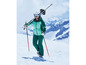 Een skiër in een groene skikleding met ski's op de schouder en skistokken in de hand.