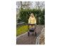 Femme âgée en veste jaune marchant avec un déambulateur sur un chemin pavé.