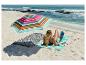 Femme lisant sur un tapis de plage CRIVIT sous un parasol coloré sur la plage.