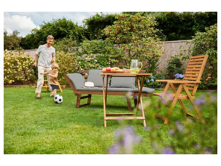 Vader en zoon spelen voetbal in de tuin met houten tuinmeubelen.