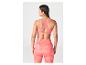 Femme de dos portant une brassière de sport rose corail et un legging à motifs.