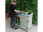 Een vrouw plant in potten op een houten tuintafel met metalen werkblad.