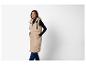 Vrouw in lange beige gewatteerde bodywarmer met capuchon, zwarte coltrui en donkere jeans