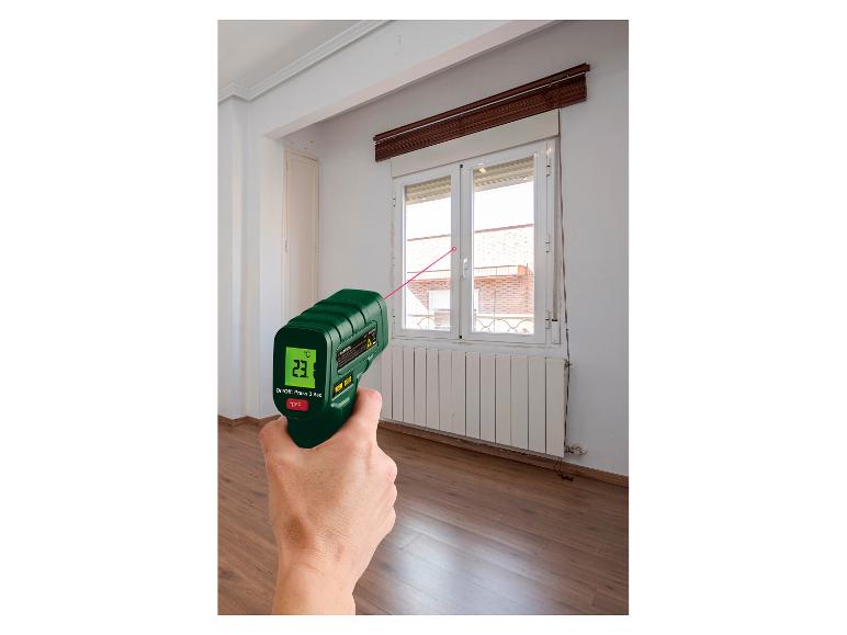 Een hand houdt een Parkside infrarood thermometer vast, die de temperatuur van een raam meet.