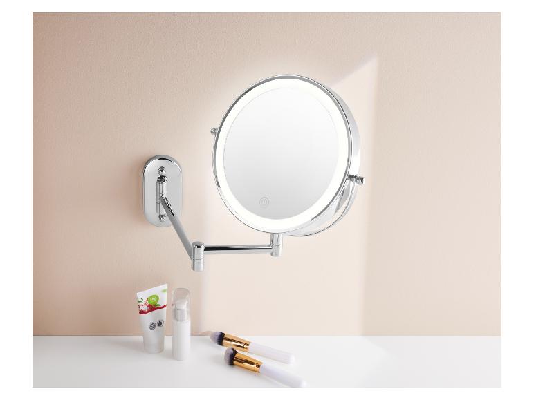 Miroir cosmétique mural avec éclairage LED, produits de beauté et pinceaux.