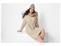 Vrouw in beige gebreide jurk, muts en sjaal, zittend.