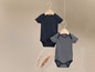 Twee baby rompers, één zwart en één gestreept, hangend aan een houten hanger.