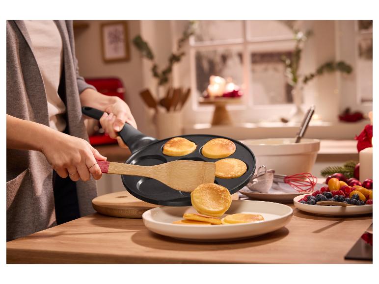 Une personne utilise une poêle à crêpes pour faire des mini-crêpes, avec des baies et des bougies en arrière-plan.