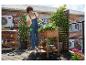 Une personne arrosant des fraisiers dans une jardinière surélevée en bois sur une terrasse sur le toit.