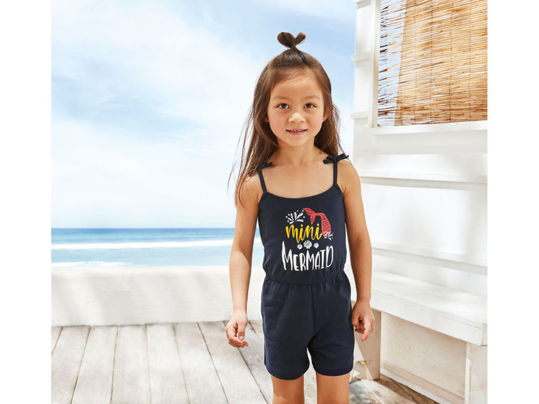 Een meisje draagt een blauwe jumpsuit met 'mini mermaid' print