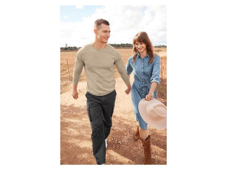 Een man en vrouw lopen hand in hand op een zandpad, zij draagt een spijkerbroekjurk en cowboylaarzen.