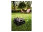 Tondeuse robot sur herbe verte avec une femme se relaxant en arrière-plan.