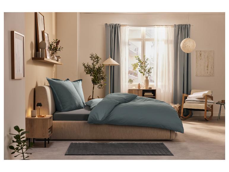 Bed met blauwgrijs beddengoed en minimalistische inrichting.