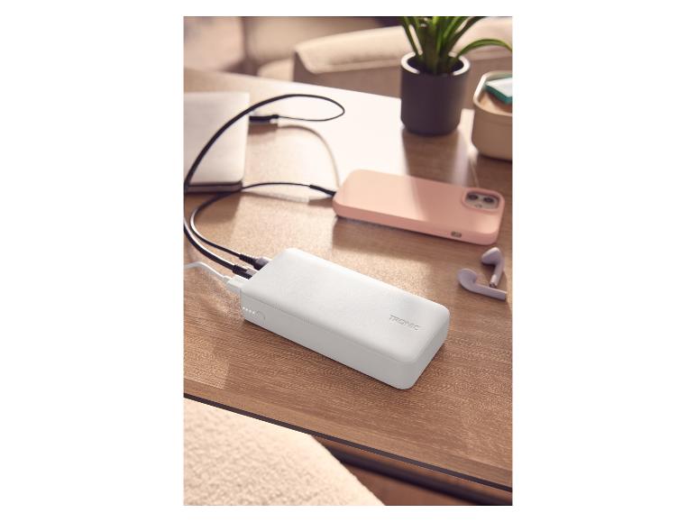 Batterie externe blanche chargeant un ordinateur portable et un smartphone sur une table en bois.