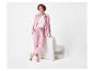 Vrouw in roze trainingspak en wit T-shirt, leunend op een witte fauteuil.