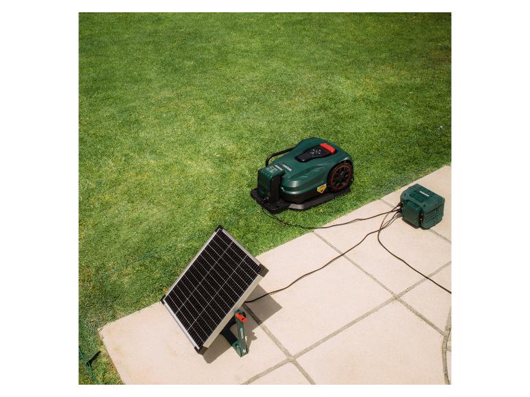 Robot tondeuse vert avec station de charge et panneau solaire dans un jardin.