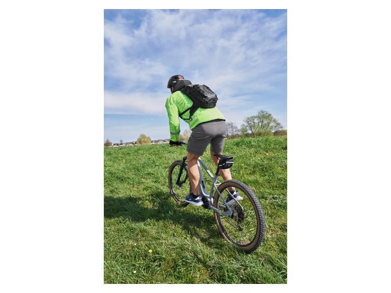 Cycliste avec un sac à dos et un maillot de vélo vert sur un VTT dans un champ herbeux.