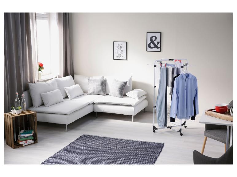 Wasrek met overhemden en broeken in een moderne woonkamer met witte bank en vloerkleed.