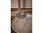 Table basse ronde en bois avec plateau gris, sur un tapis blanc.