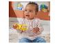 Bébé heureux jouant avec un hochet singe jaune, assis sur un tapis avec des jouets en arrière-plan.