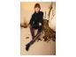 Vrouw in zwarte turtleneck trui en bordeauxrode leren leggings zit op een rots.