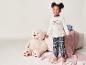 Une fille en pyjama à carreaux et avec un t-shirt qui dit 'Make your own magic', à côté d'un ours en peluche.
