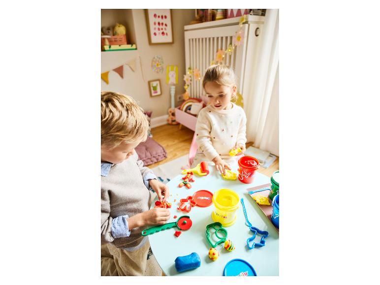 Twee kinderen spelen met klei en vormpjes aan een blauwe tafel.