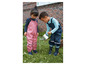 Deux enfants dans le jardin avec des salopettes imperméables et des bottes.