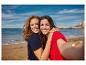 Deux femmes souriantes en t-shirts sur une plage, prenant un selfie.