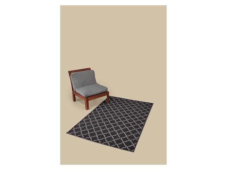Fauteuil en bois avec coussins gris et tapis noir à motif géométrique.