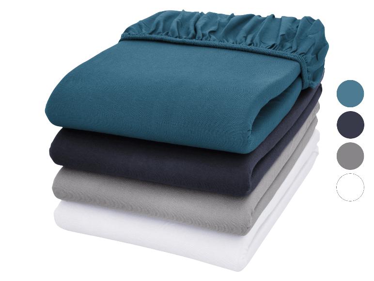 Gestapelde hoeslakens in blauw, marineblauw, grijs en wit met kleurstalen.