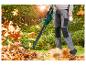 Persoon gebruikt een bladblazer om herfstbladeren in een tuin op te ruimen.