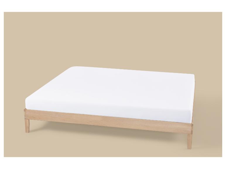 Eenvoudig licht houten bedframe met een wit matras op een beige achtergrond.