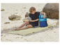 Een vrouw op een strand met een Mistral koelbox en een gestreepte strandlaken.