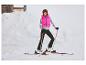 Lachende vrouw in roze vest en ski-uitrusting in de sneeuw.