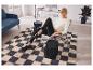 Femme assise dans un fauteuil moderne avec un sac à dos noir à côté, sur un tapis à motifs.