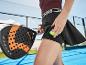 Vrouw op padelbaan met racket en bal in zak, gekleed in sporttop en rok.